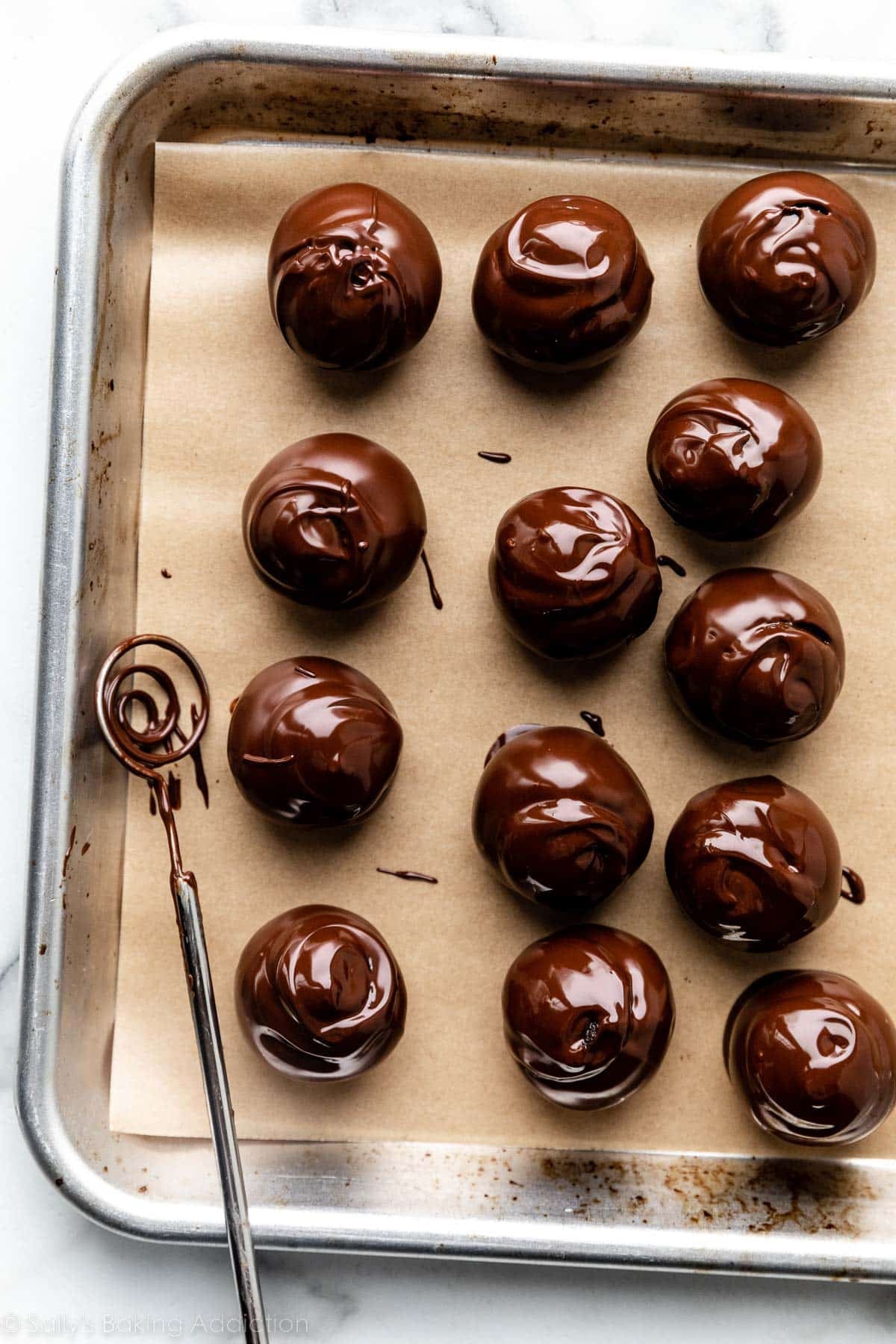 baking tray with just-dipped chocolate covered truffles arranged on it.