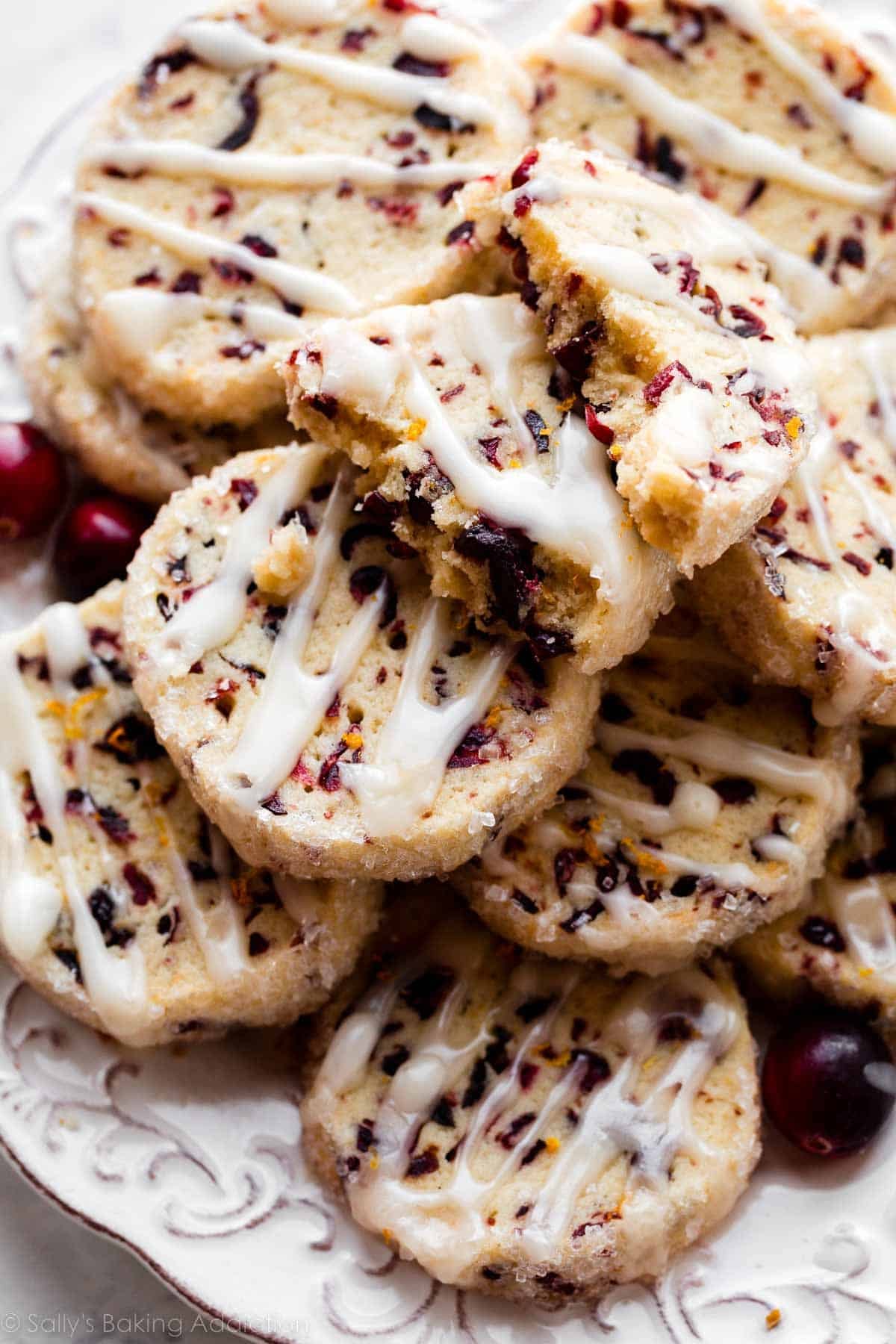 plate of dried cranberry cookies with icing on top and one cookie broken in half.