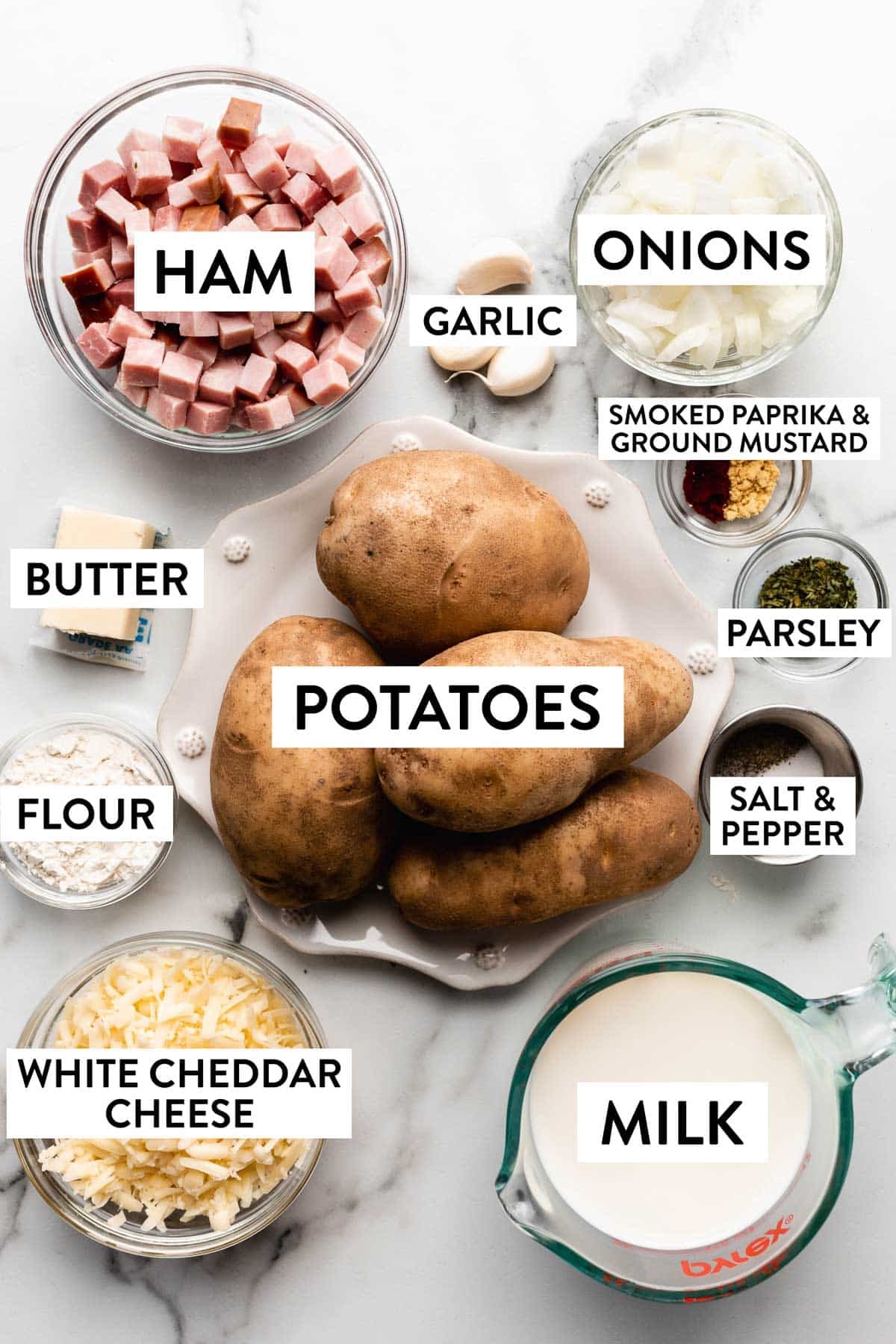 ingredients on counter including ham, white cheddar cheese, potatoes, herbs, milk, flour, butter, and chopped onions.