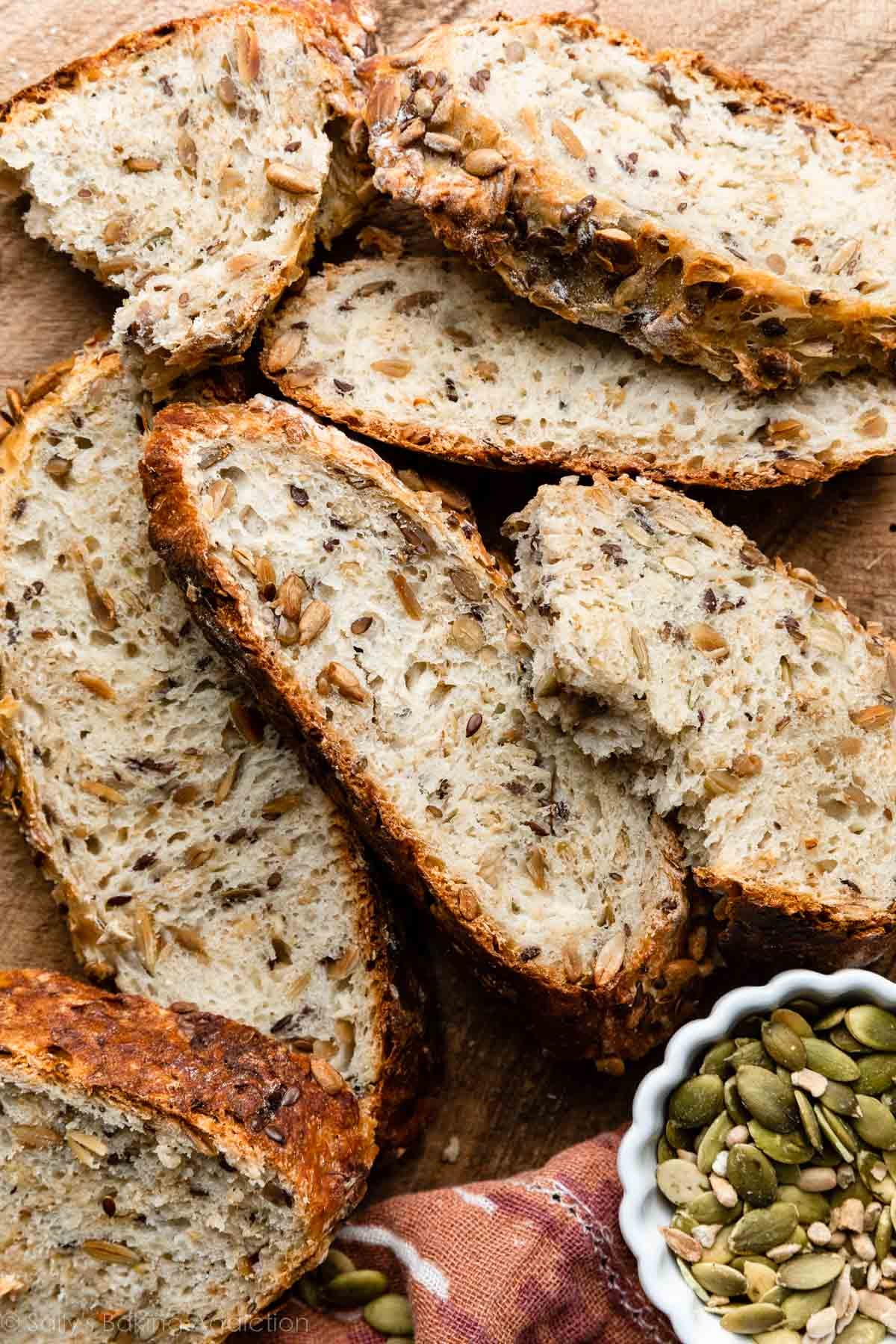 sliced seeded bread with brown crust on wooden cutting board.