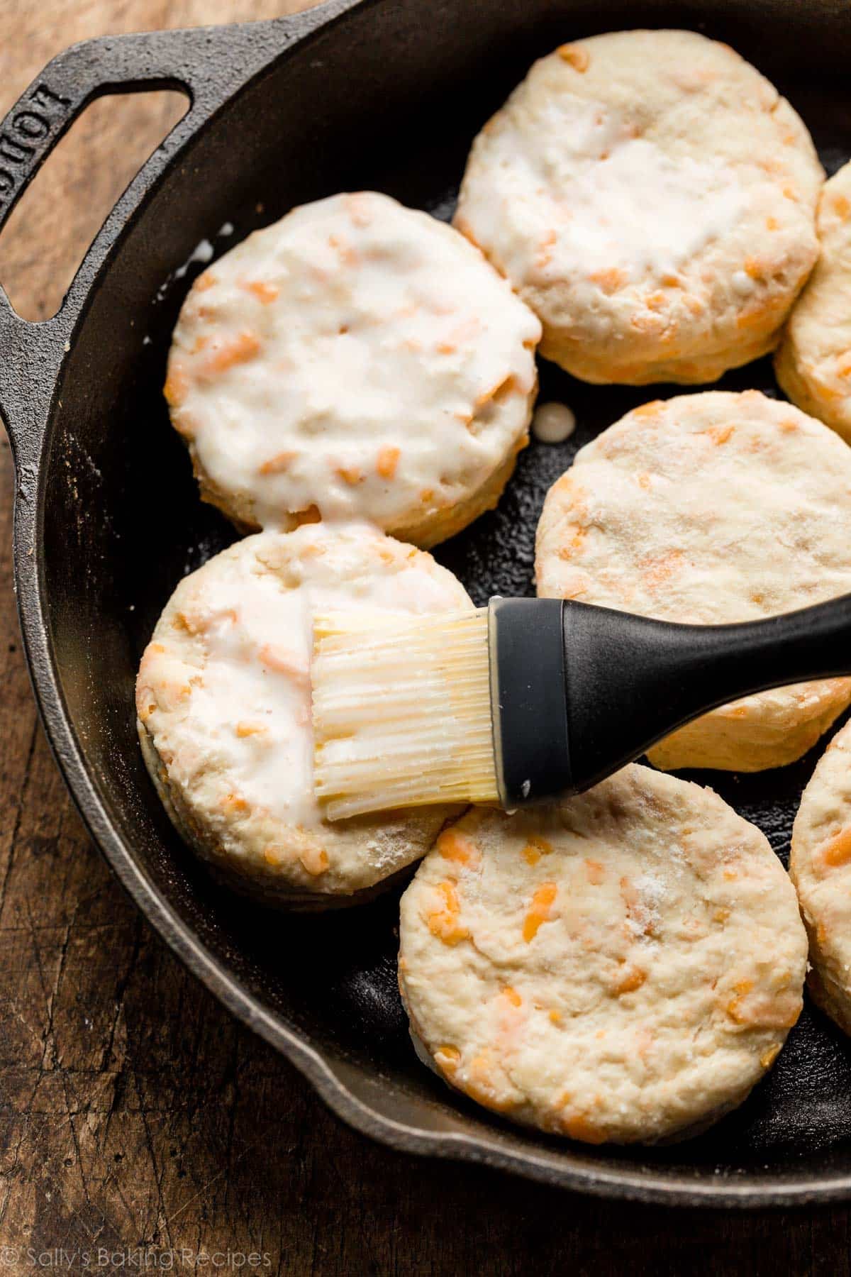 pastry brush brushing milk on top of shaped unbaked biscuits.