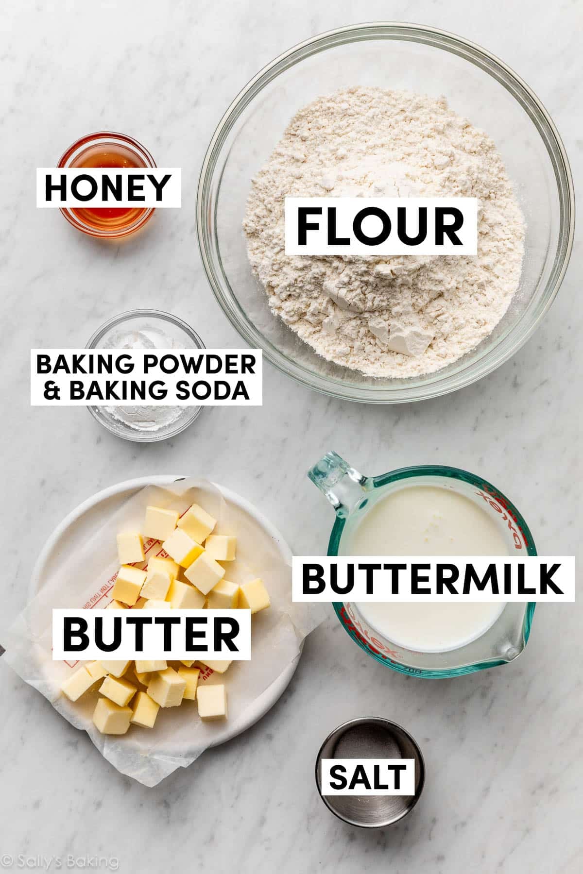 ingredients on marble counter including butter, buttermilk, flour, and honey.