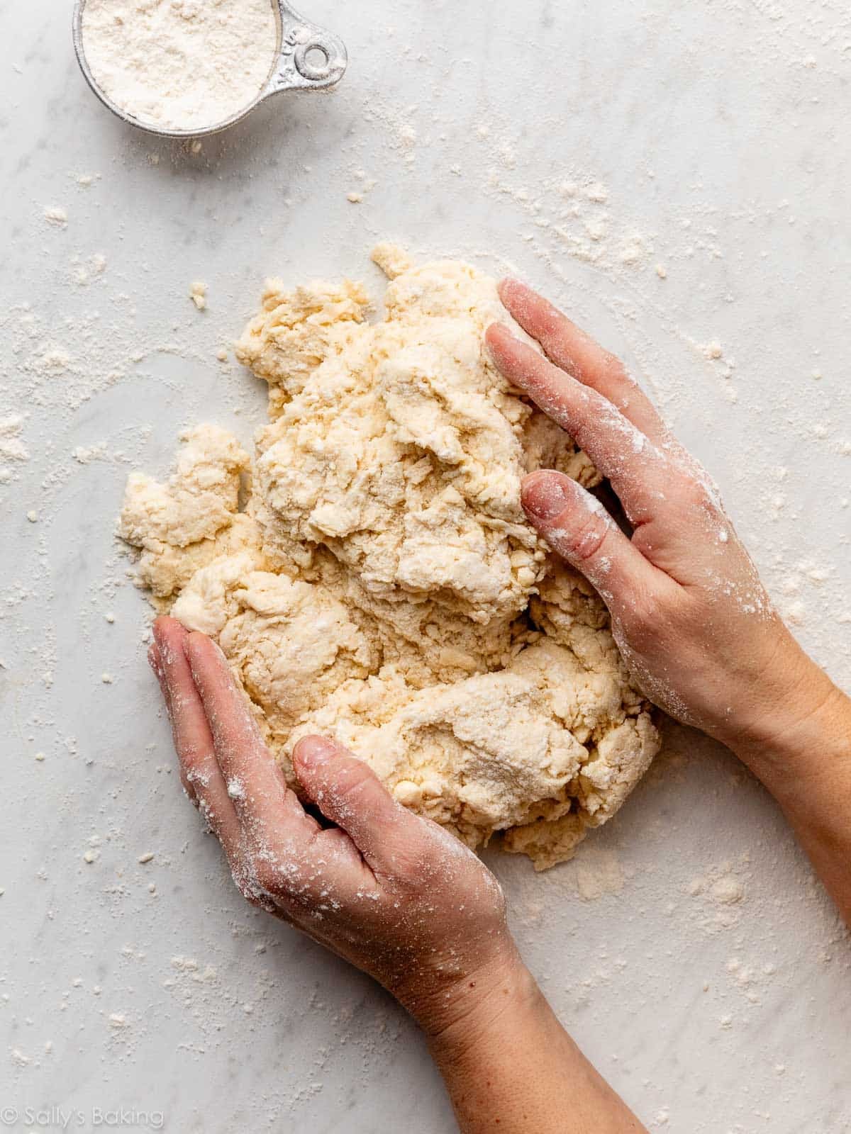 hands gathering dough together on marble surface.