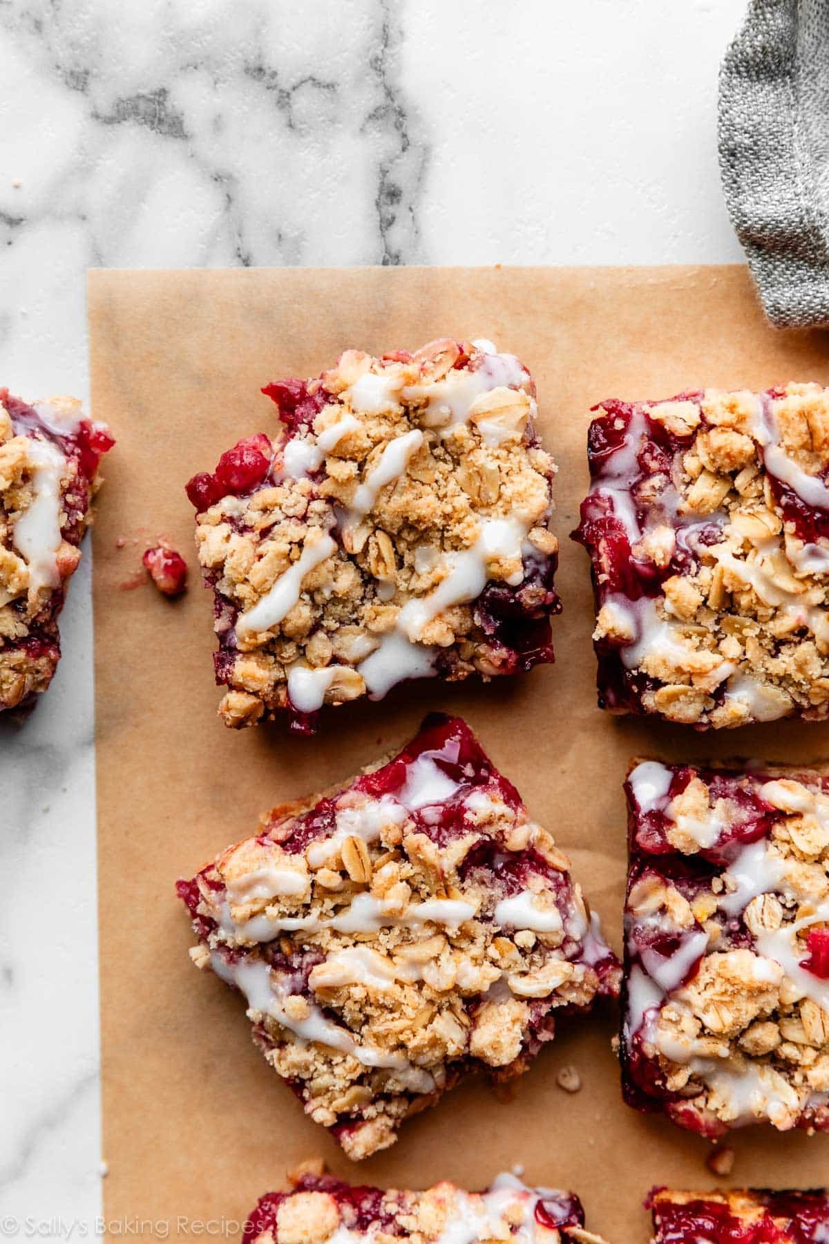 cherry pie bars with crumb topping and white icing on top on brown parchment paper.