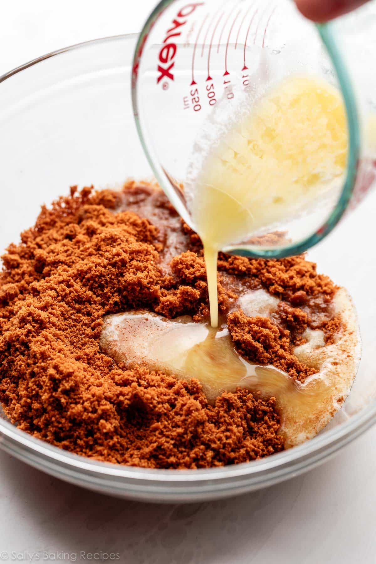 pouring melted butter on top of cookie crumbs in glass bowl.