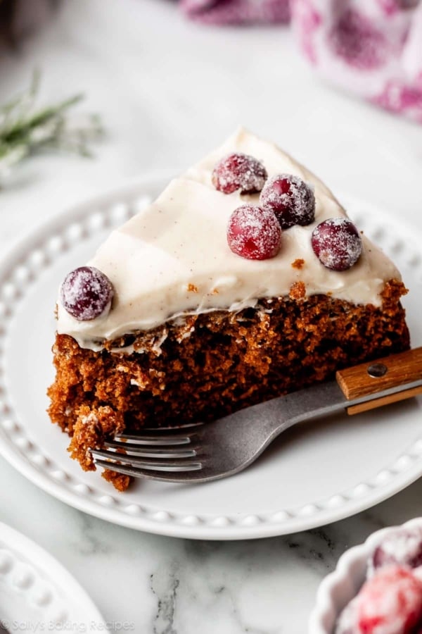 slice of gingerbread cake with cream cheese frosting on top and sugared cranberries.