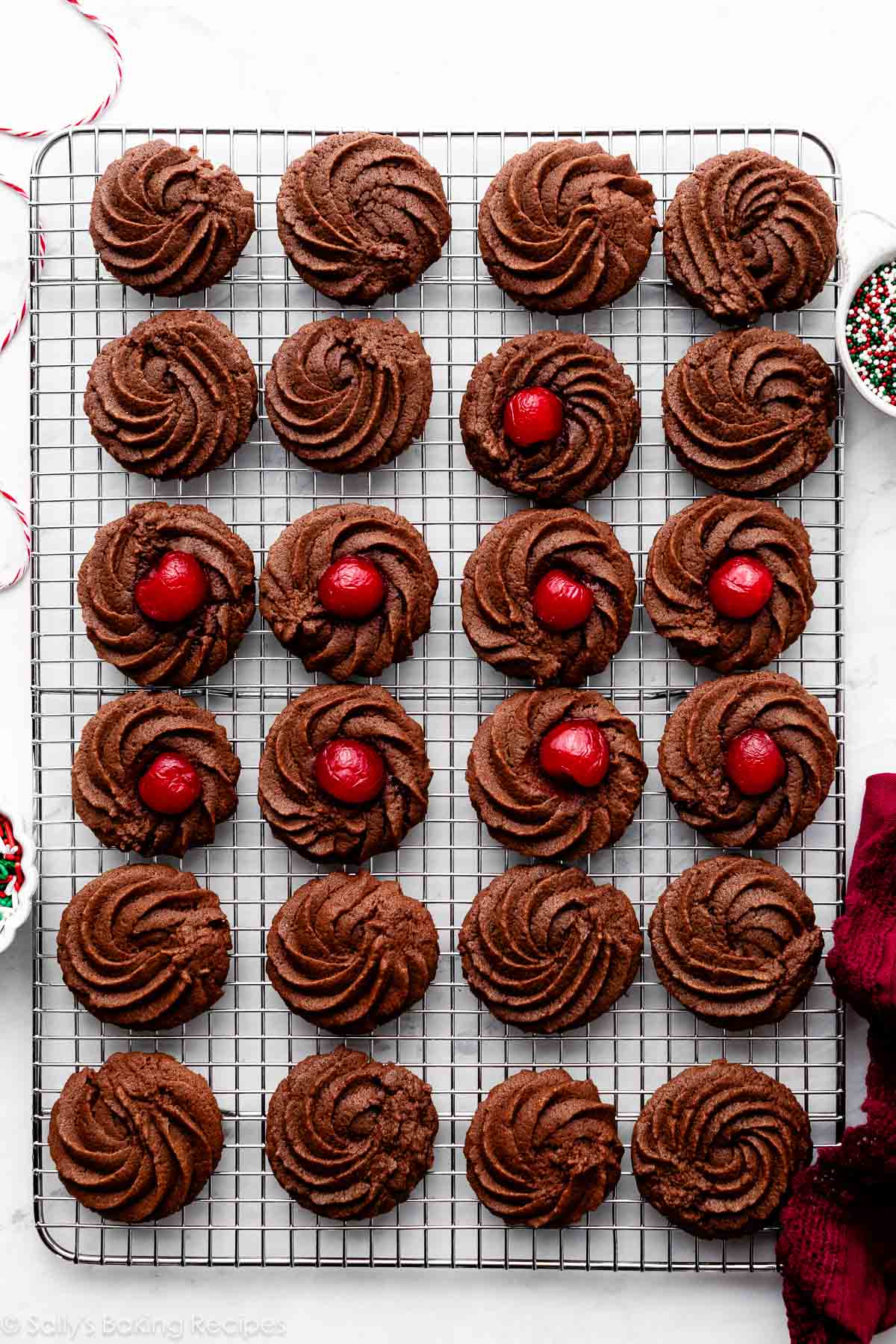piped chocolate cookies on cooling rack with some with cherry baked in center.