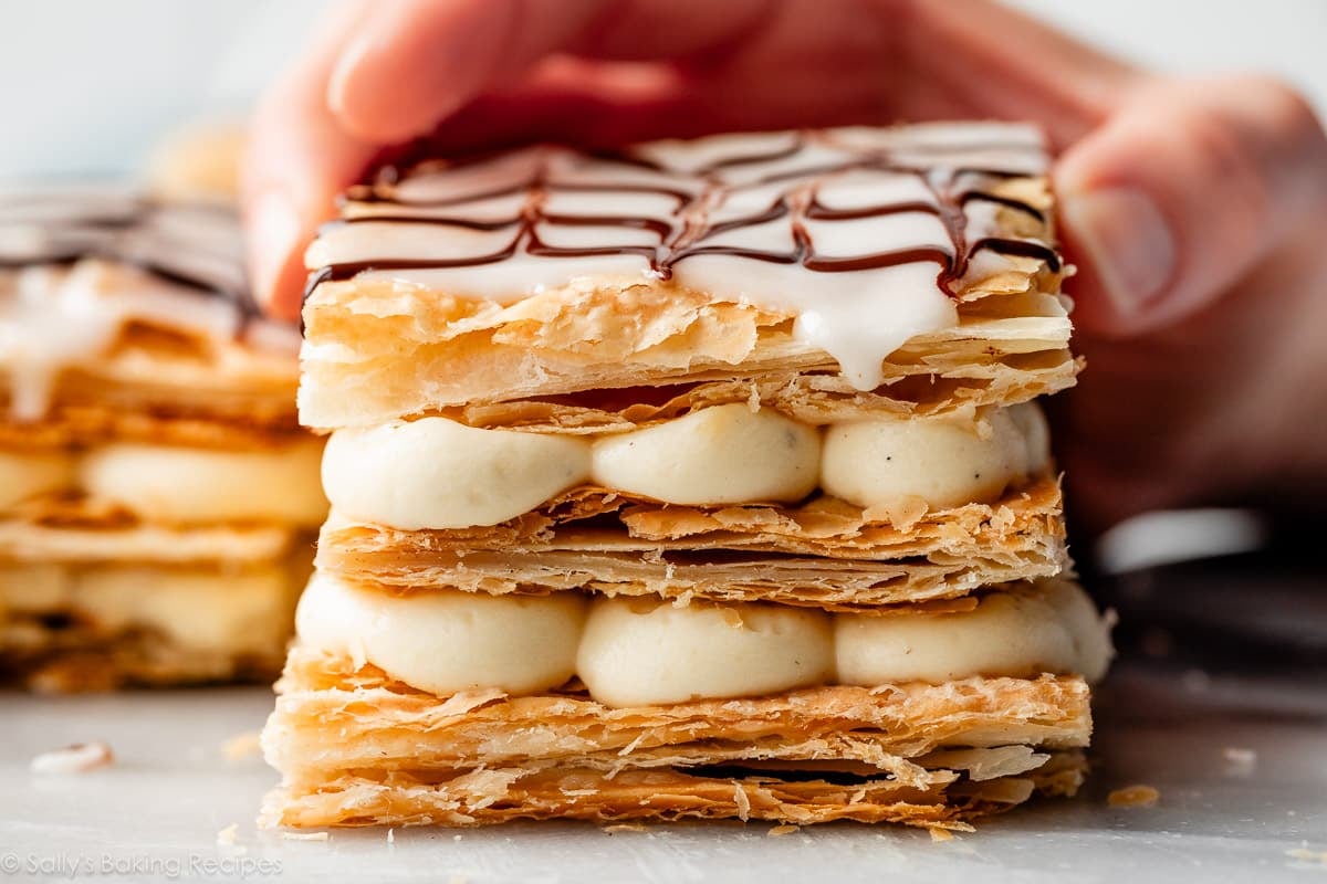 hand placing the icing-topped pastry square on top of the other two layers of pastry cream.