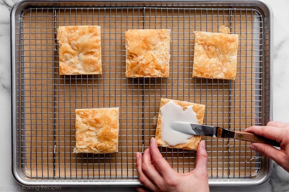 hand spreading vanilla icing on baked puff pastry pieces.
