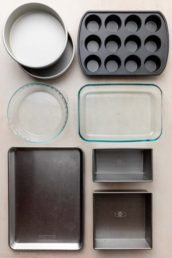 baking pans on beige surface including a muffin pan, square pan, baking sheet, glass pie dish, glass rectangle dish, and metal cake pans.