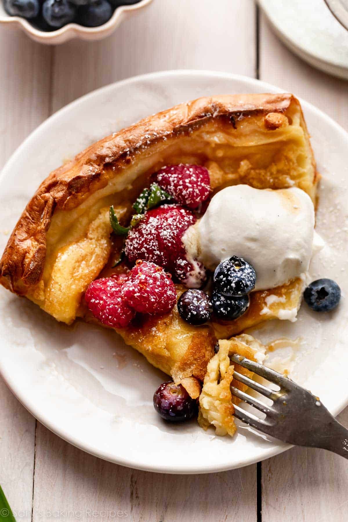 dutch baby slice on plate with berries and whipped cream.