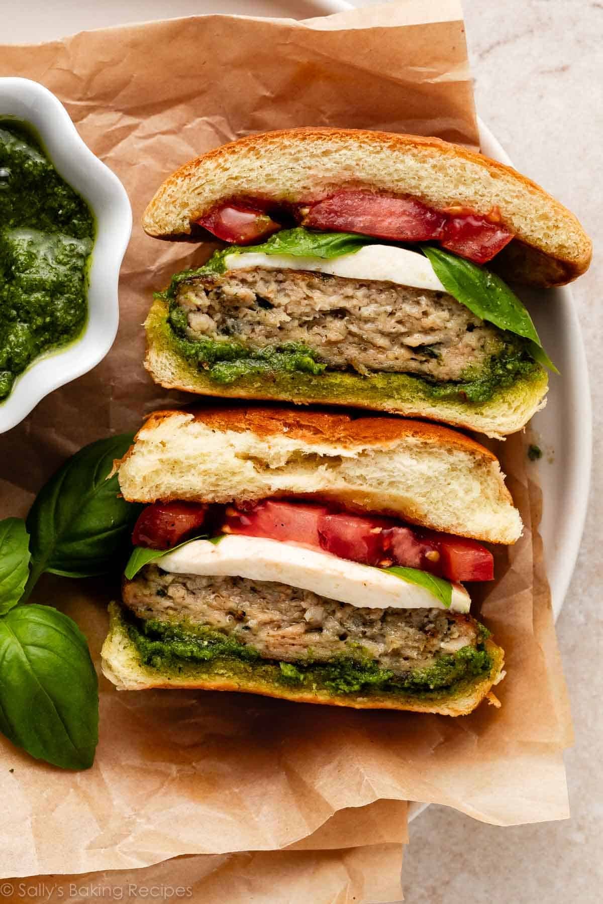 caprese pesto chicken burger with tomato and basil cut in half and face up.
