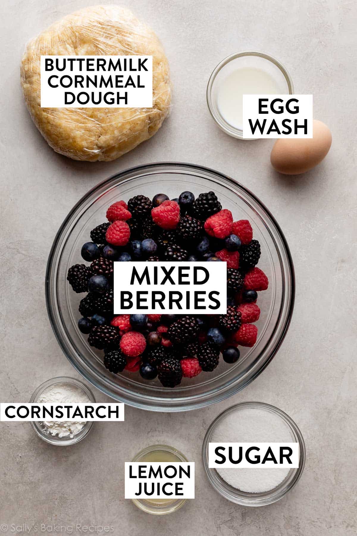 mixed berries in bowl with other ingredients on counter including egg, sugar, lemon juice, and cornstarch.