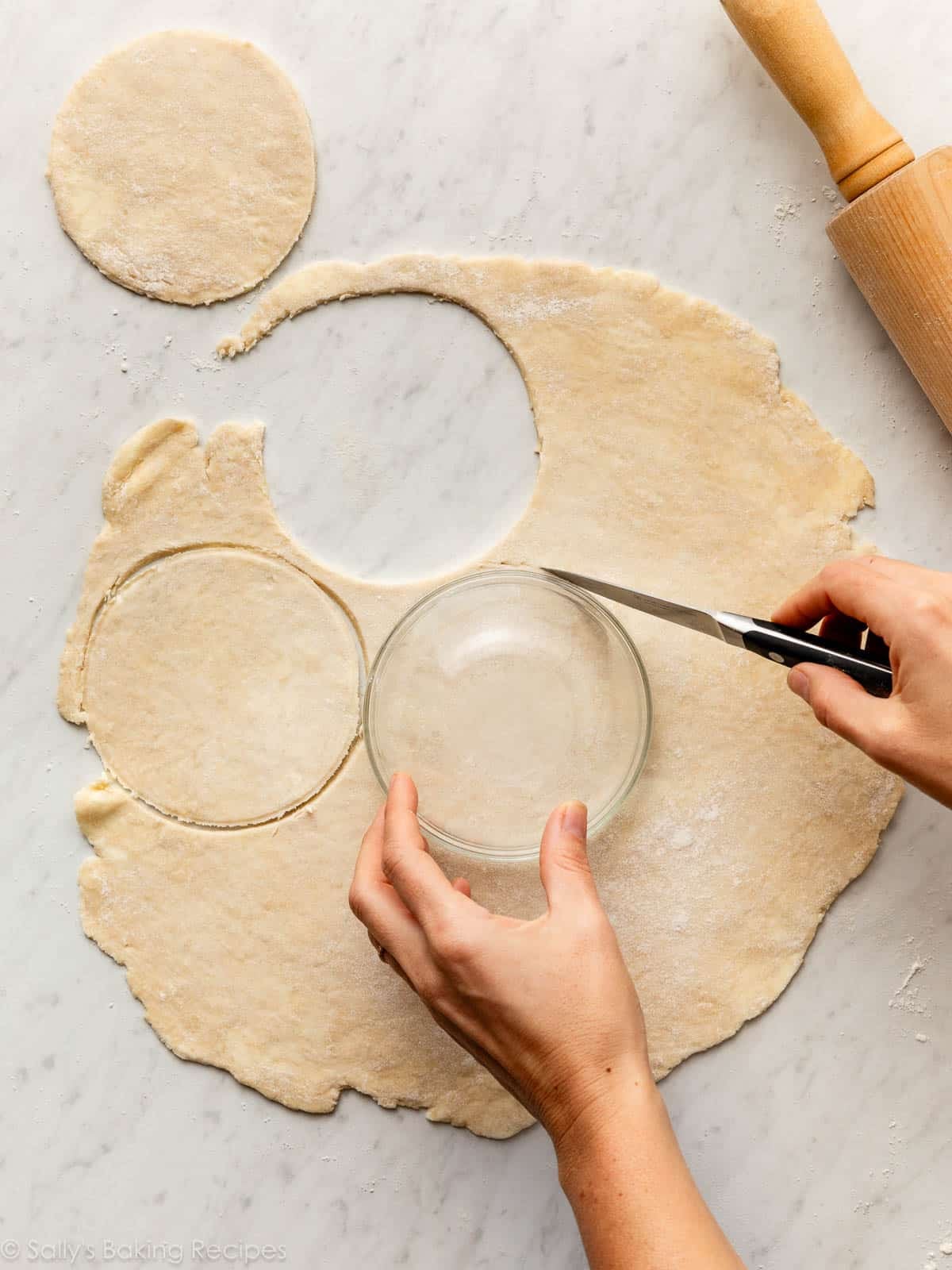 cutting circles into rolled out pie dough using a bowl and knife.