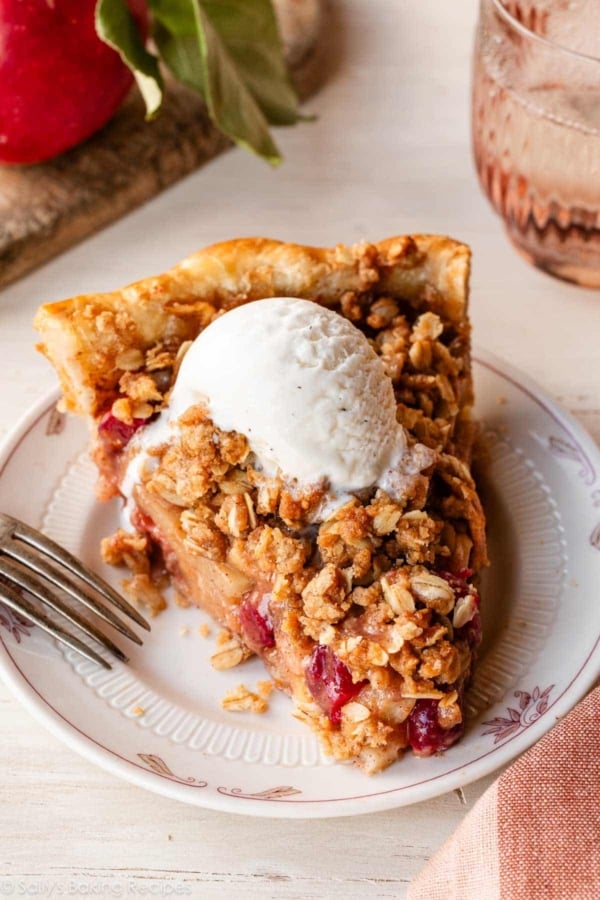 slice of apple cranberry crumble pie with vanilla ice cream on white plate.