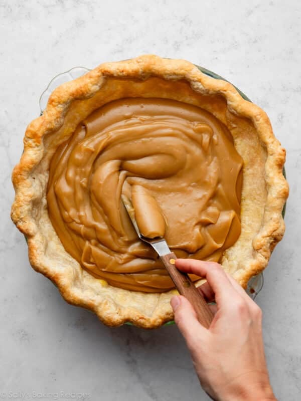 hand spreading butterscotch filling into baked pie crust.