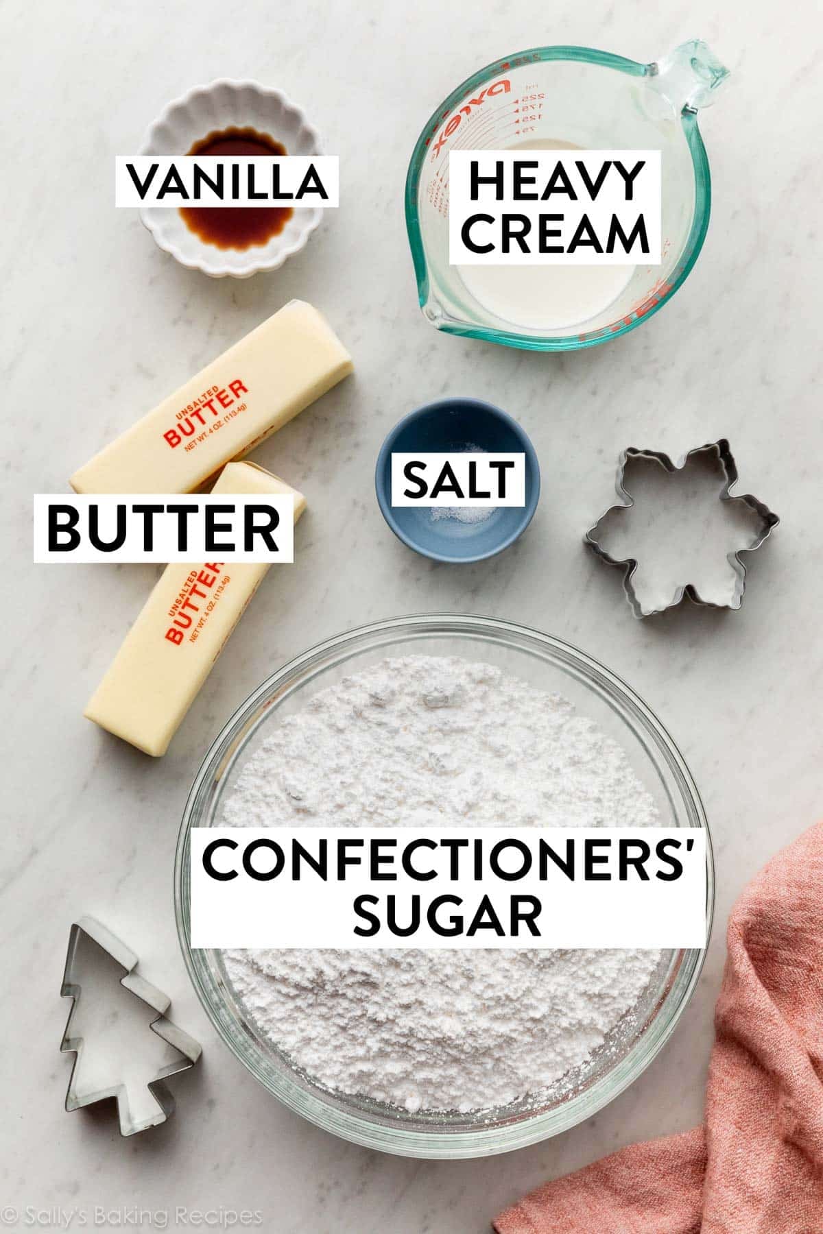 ingredients on a marble counter including confectioners' sugar, heavy cream, butter, and vanilla.