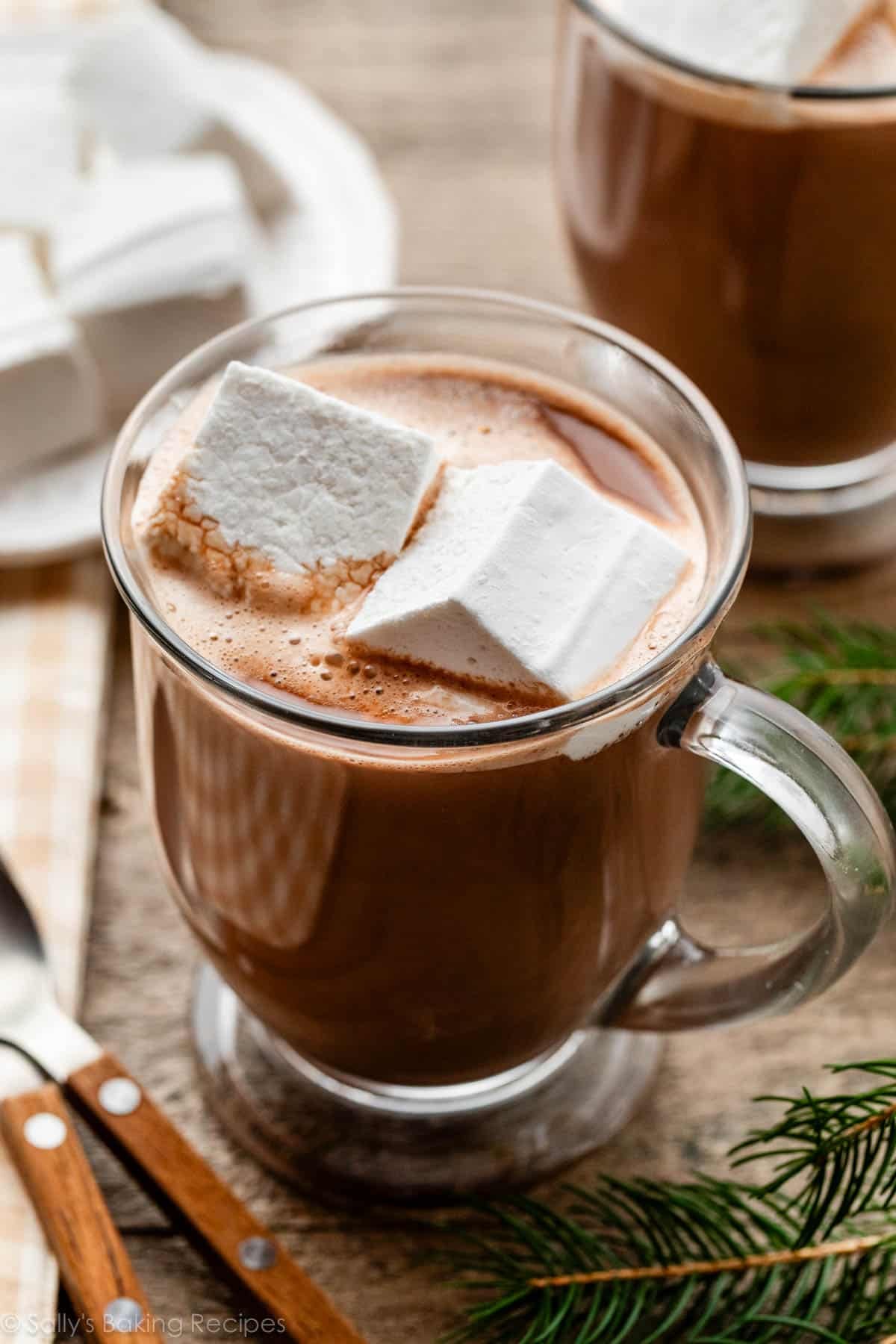 two square homemade marshmallows in a glass mug of hot chocolate.