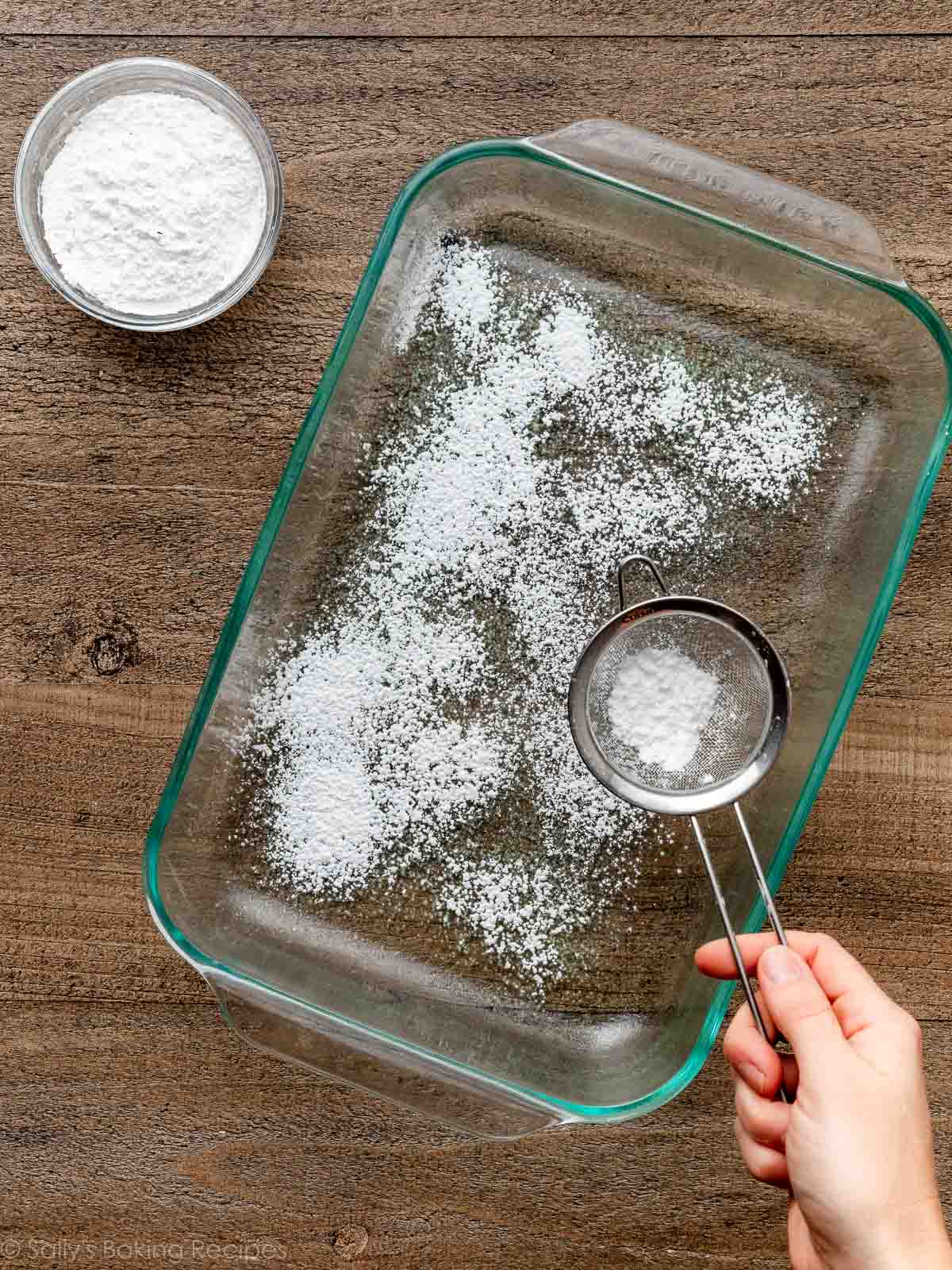 sifting confectioners' sugar and cornstarch in a glass pan.