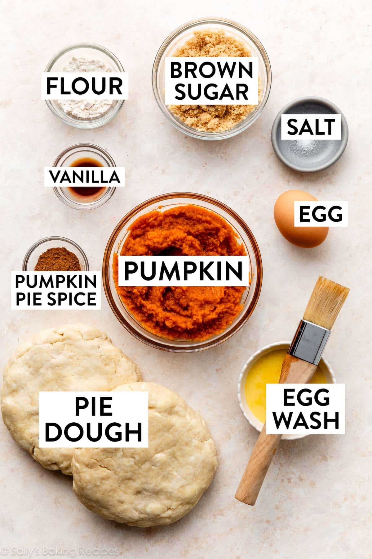 ingredients on beige surface including pie crust, brown sugar, flour, spices, and egg wash.