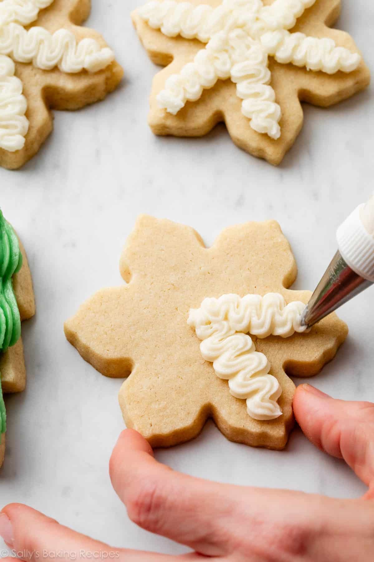 hand piping squiggles of buttercream on top of snowflake-shaped cookie.