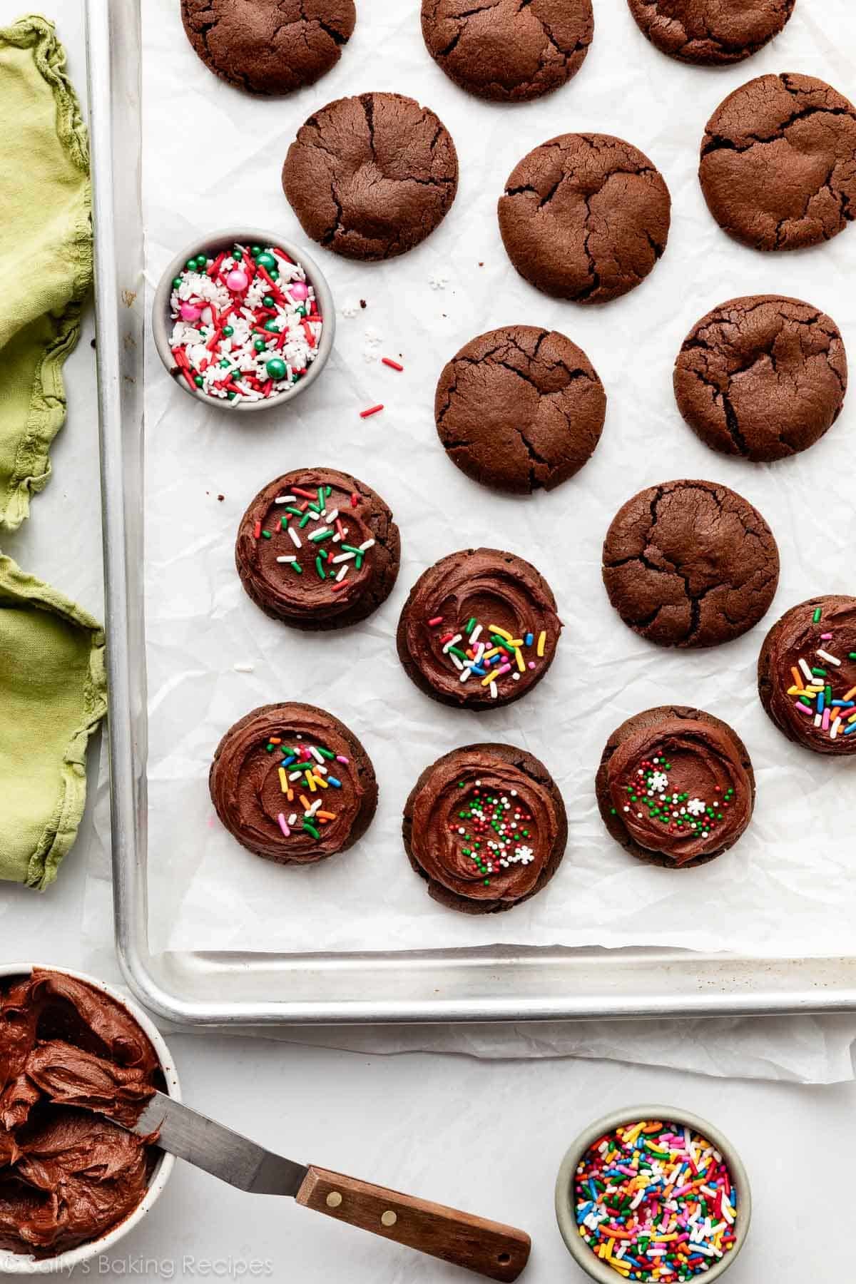 chocolate cookies with frosting and sprinkles on parchment paper lined baking sheet.