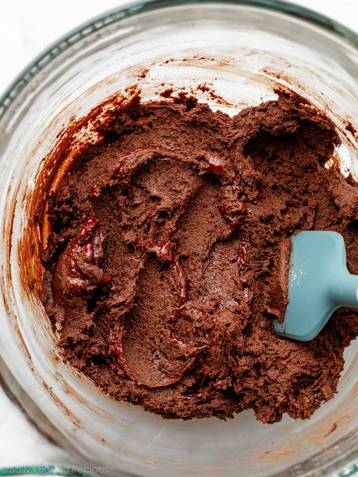 chocolate cookie dough with blue spatula in glass bowl.