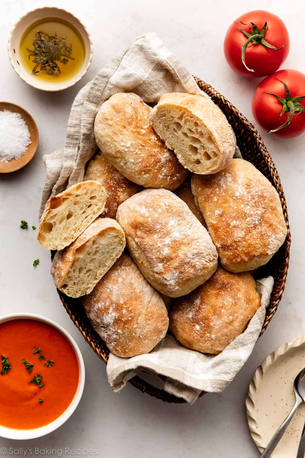 ciabatta rolls in basket with tomatoes, soup, and small bowl of dipping olive oil next to it.