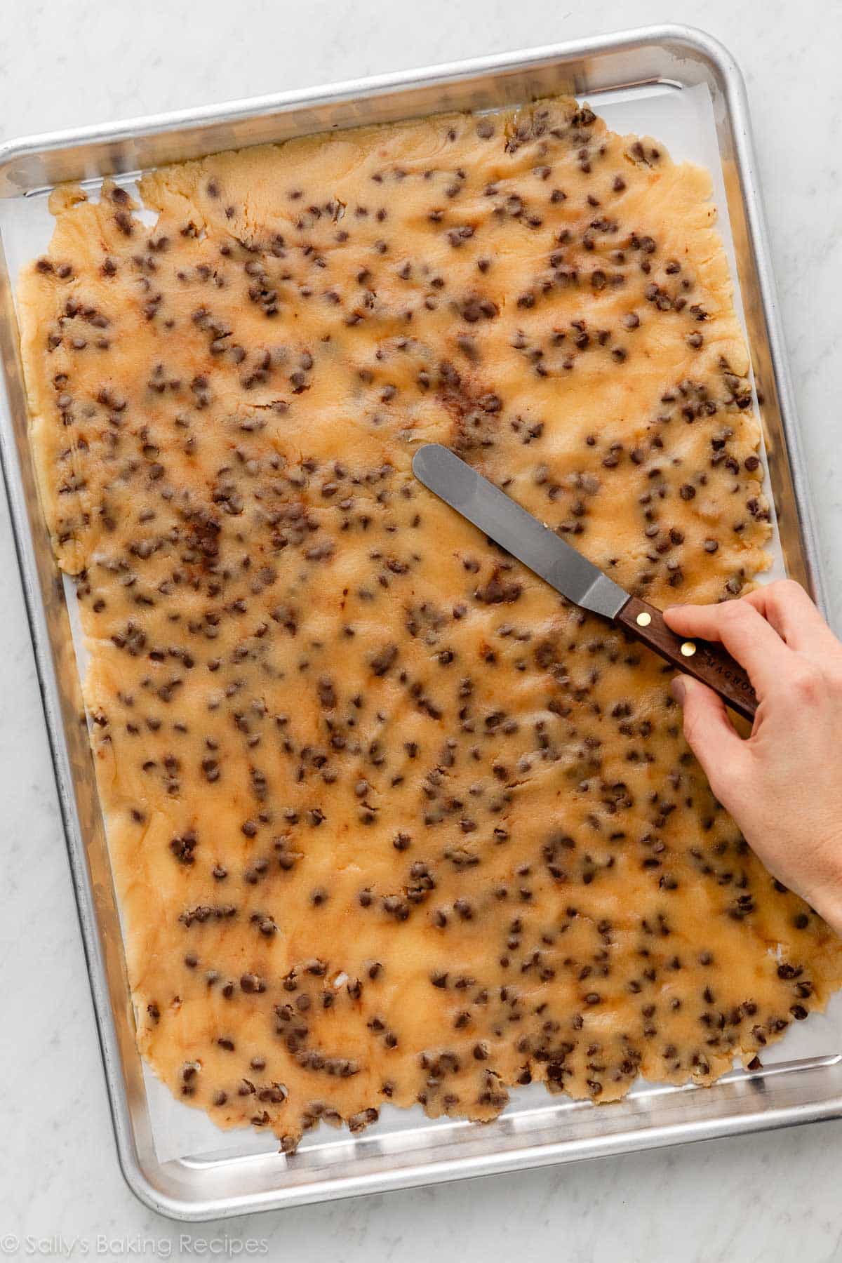 hand spreading cookie dough in a thin layer on a rimmed baking sheet.