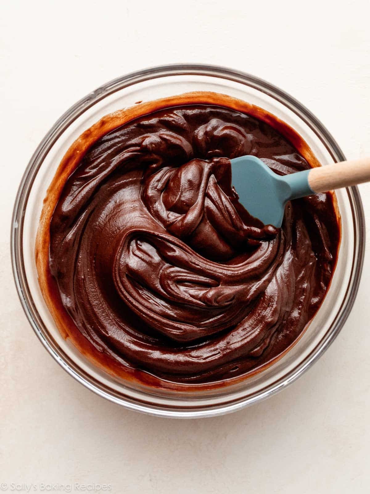 creamy chocolate fudge in glass bowl with blue spatula.