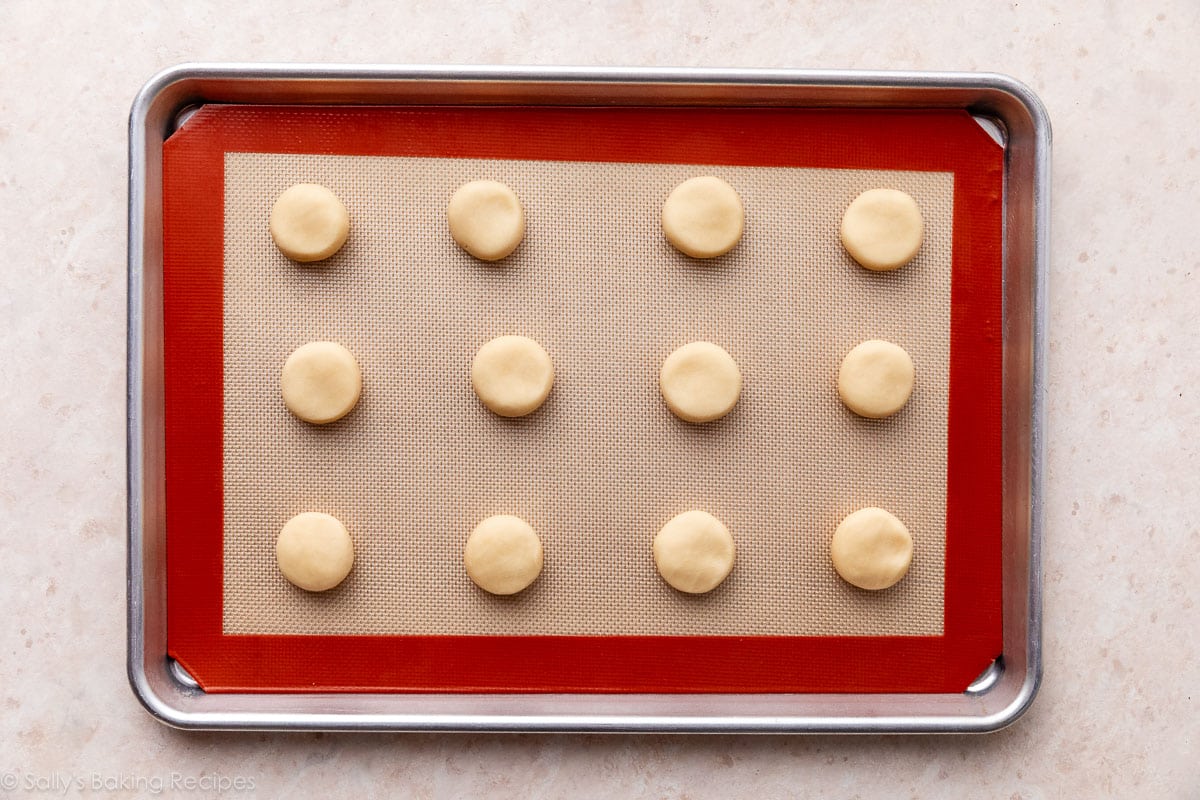 12 flattened dough balls on silicone baking mat-lined baking sheet.