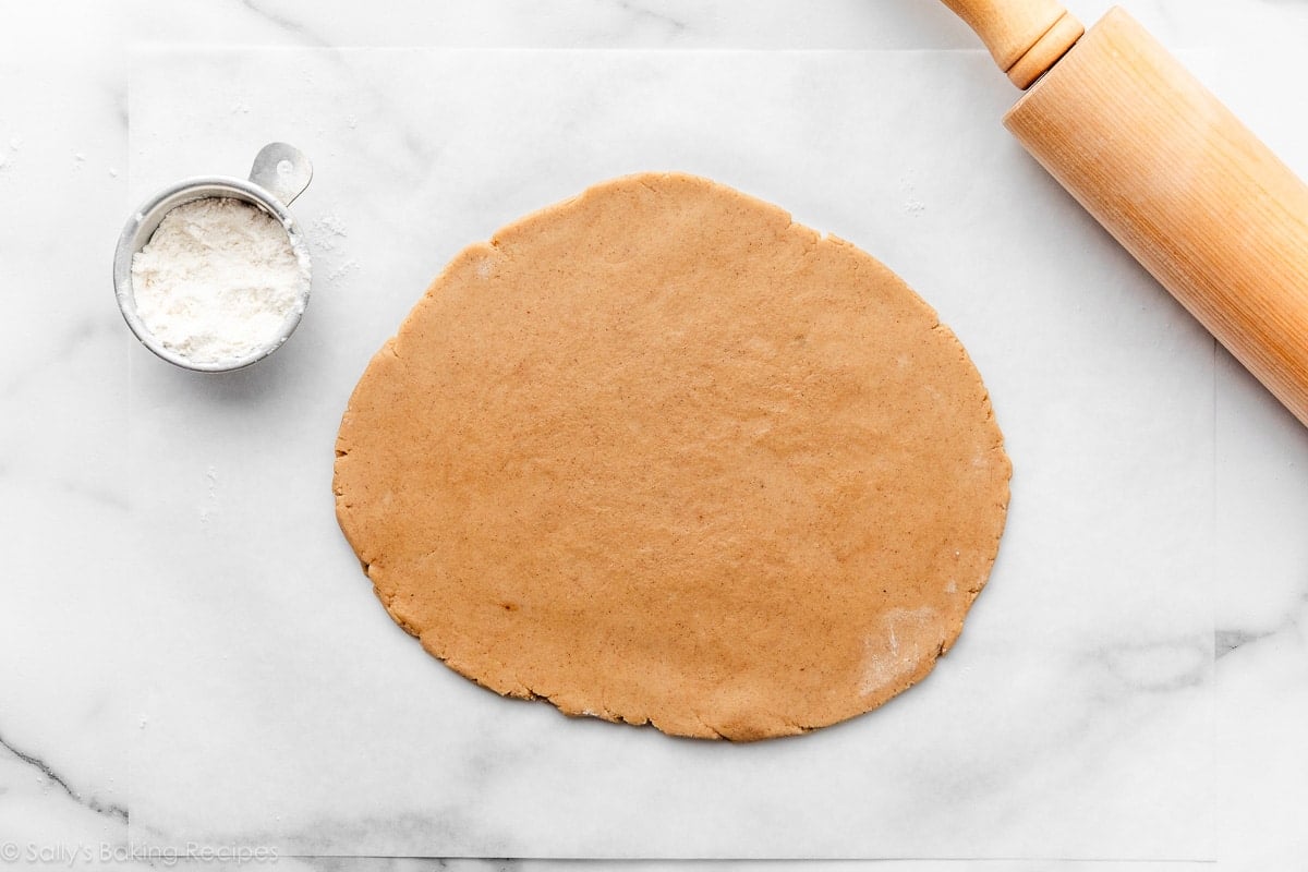 brown sugar cookie dough on white parchment paper with rolling pin in the corner.