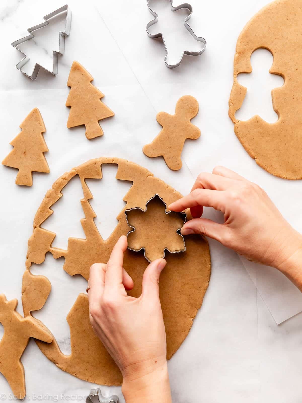 hands using Christmas-shaped cookie cutters on brown sugar cookie dough.