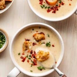 2 bowls of cauliflower potato soup with croutons, bacon, and chopped chives on top.