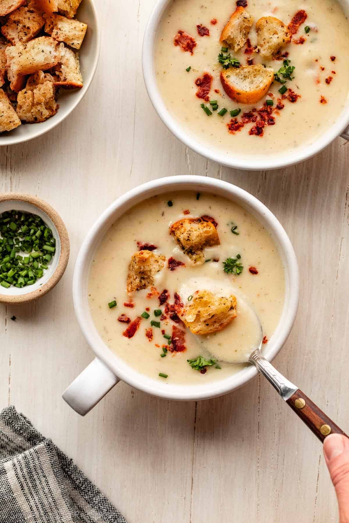 2 bowls of cauliflower potato soup with croutons, bacon, and chopped chives.