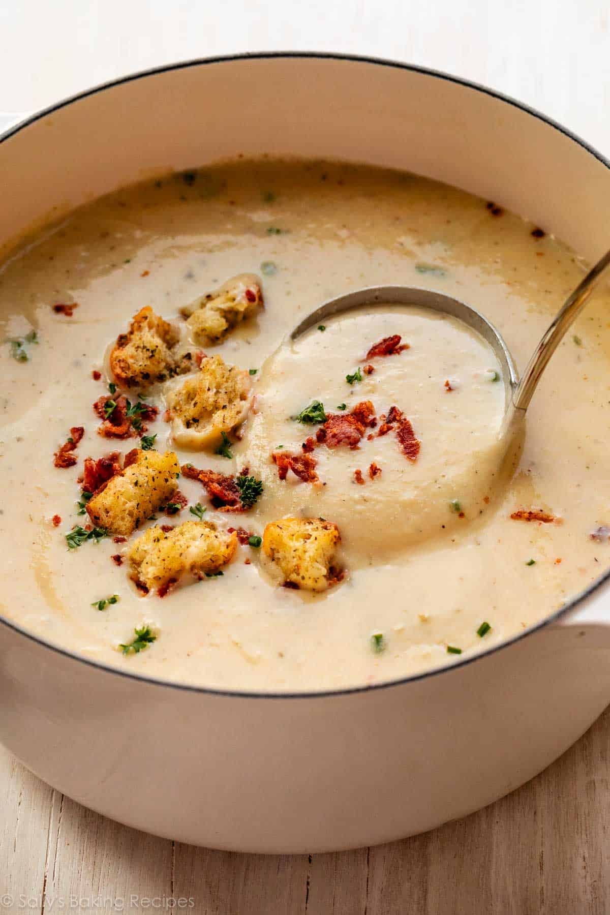 pot of creamy cauliflower potato soup with bacon, chives, parsley, and croutons on top.