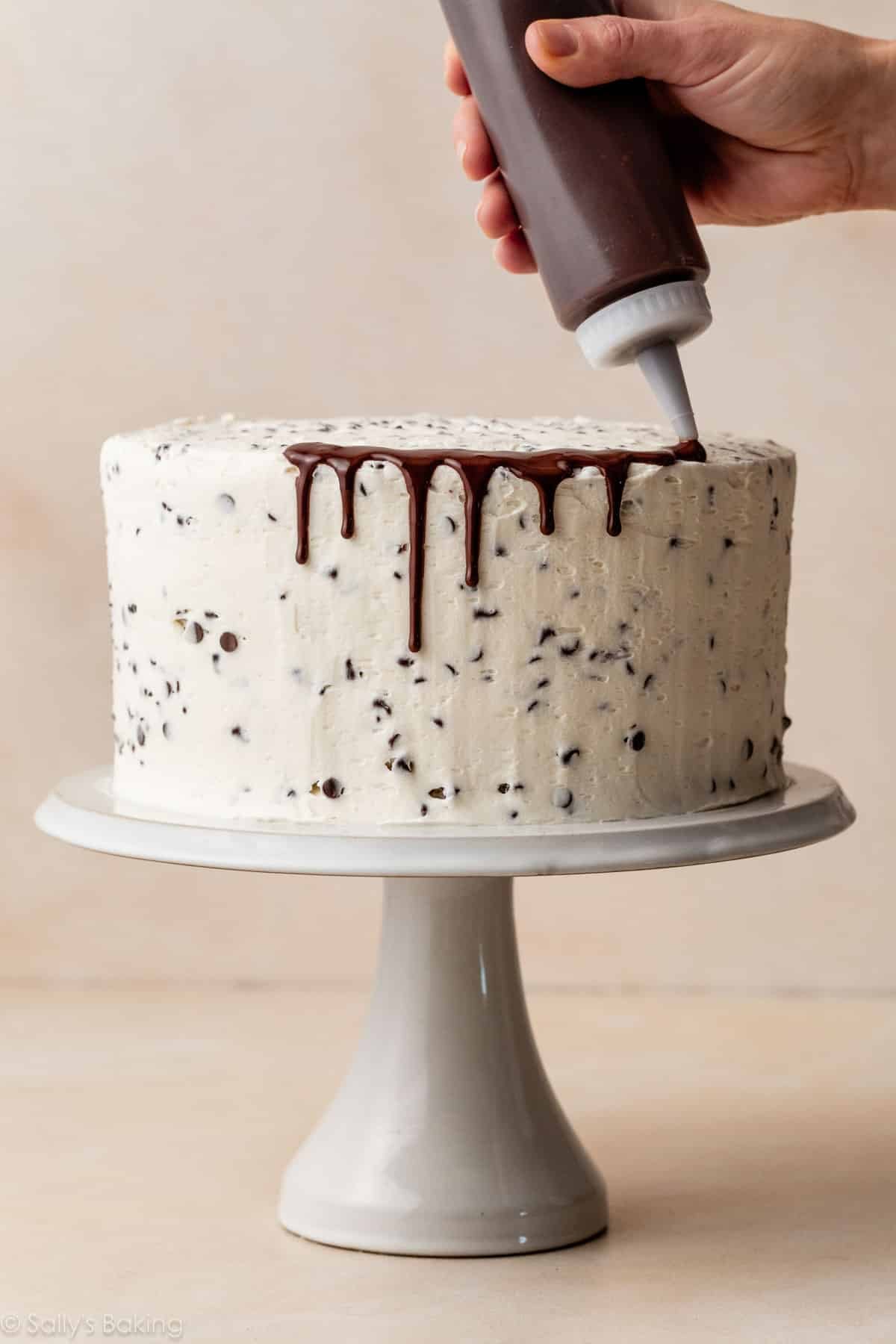 squeeze bottle applying chocolate ganache drip down the sides of frosted layer cake.