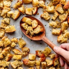 wooden spoon with homemade croutons on parchment paper lined-baking sheet.