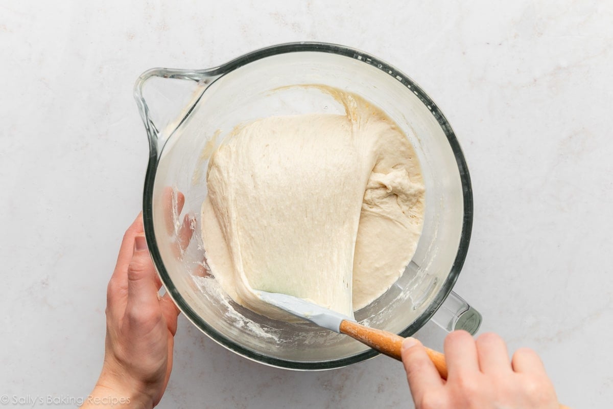 spatula pulling dough down over itself in glass bowl.