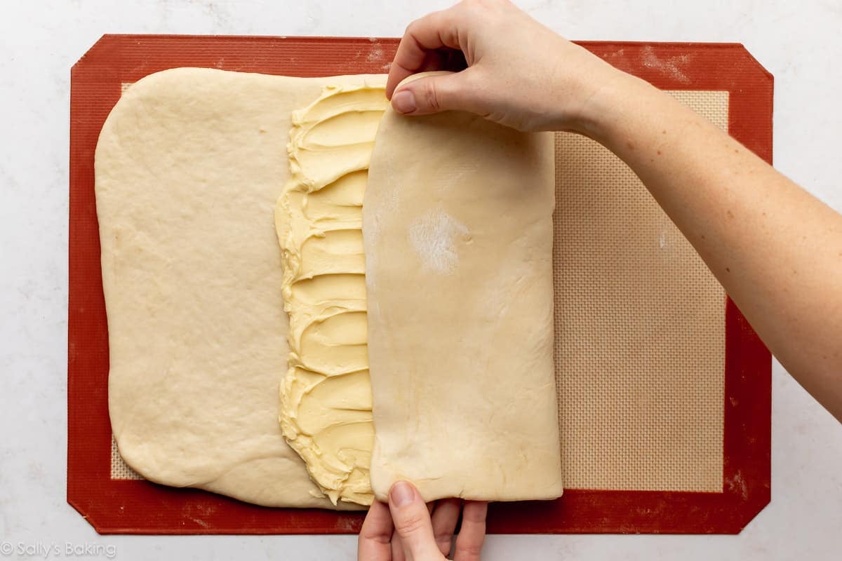 hands folding dough over lamination butter layer on top of silicone baking mat.