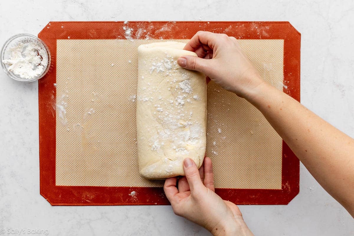 hands folding dough over itself on top of silicone baking mat.
