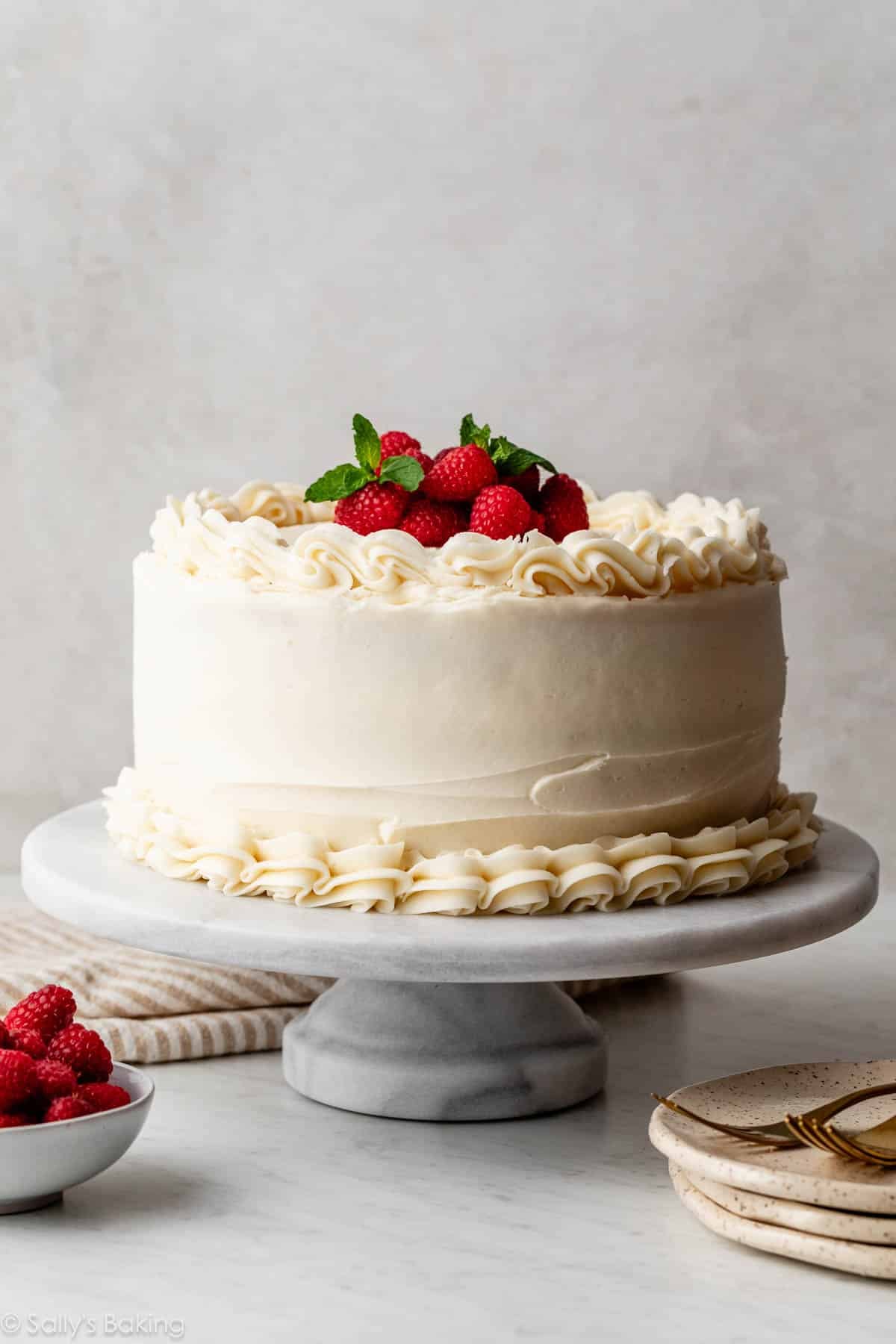 vanilla layered cake with piped vanilla frosting and fresh raspberries and mint on top.