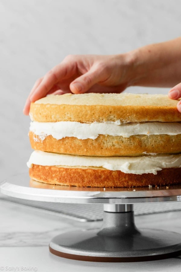 hands placing 3rd cake layer on top of a cake.
