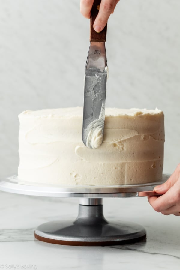 spreading vanilla frosting on layer cake with an icing spatula.