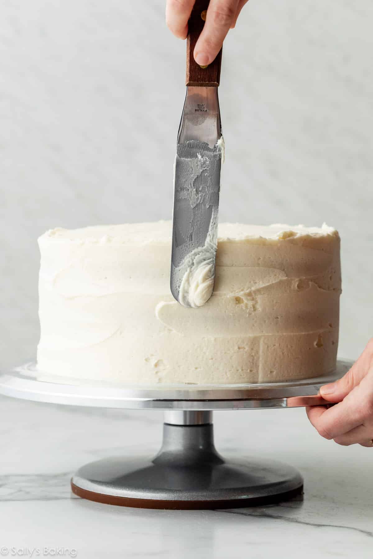 spreading vanilla frosting on layer cake with an icing spatula.