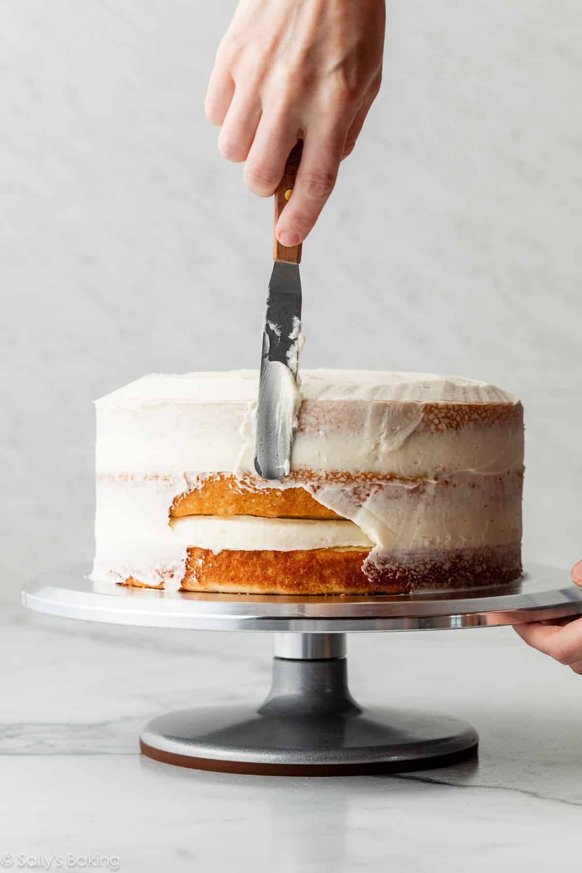 hand spreading crumb coat of frosting on layer cake.