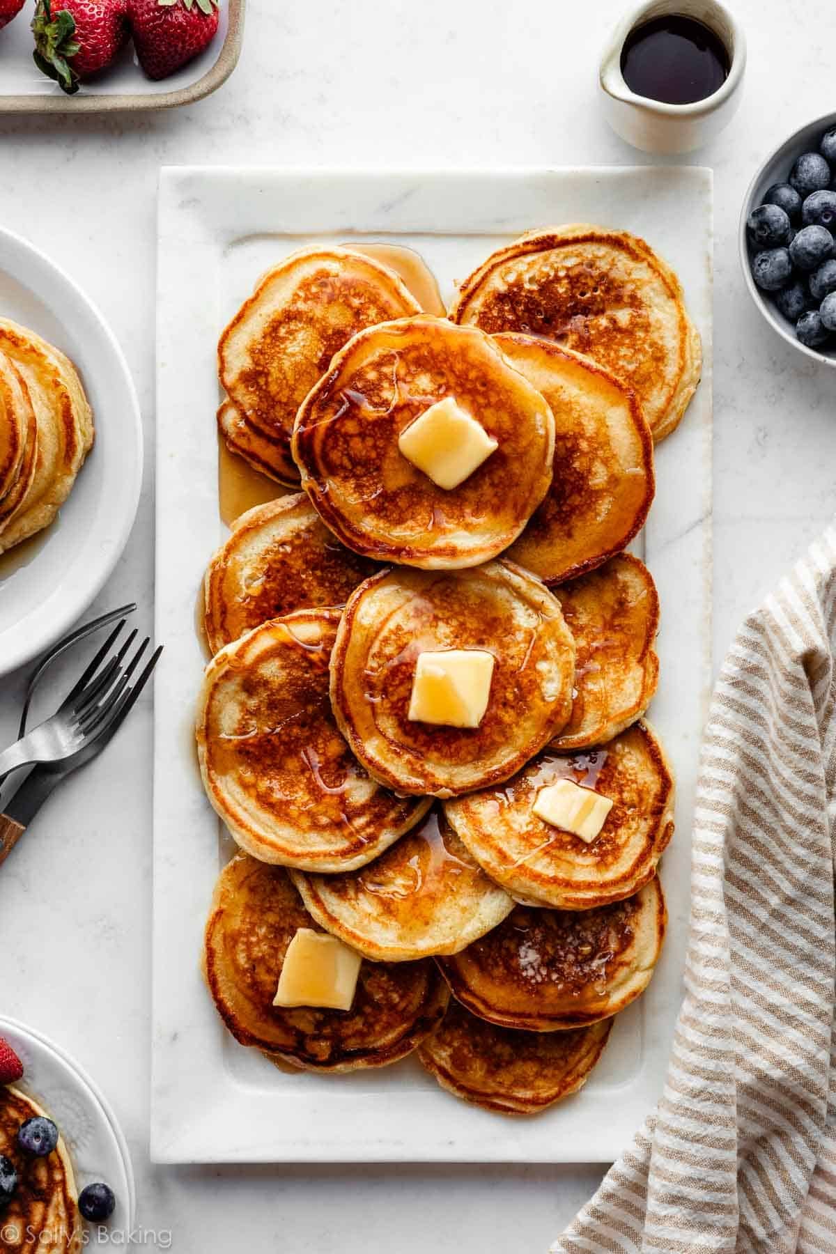 platter of pancakes with butter and maple syrup on top.