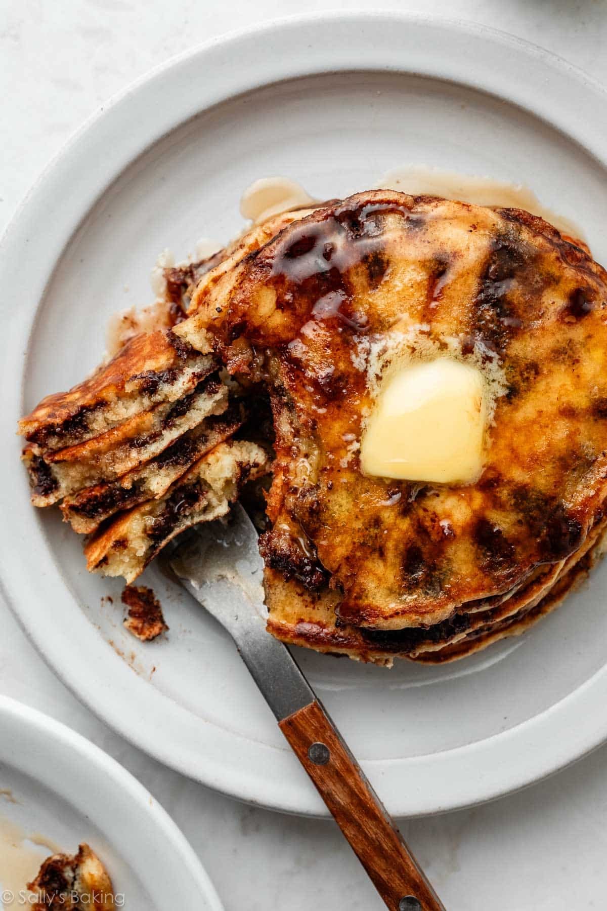chocolate chip pancakes with butter and maple syrup on a white plate.