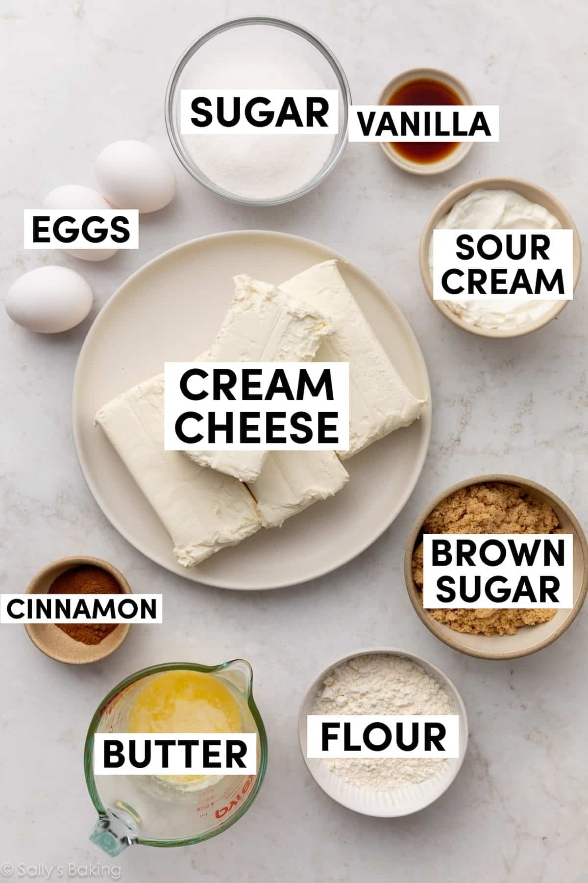 ingredients on marble surface including cream cheese, sour cream, brown sugar, eggs, melted butter, flour, and cinnamon.