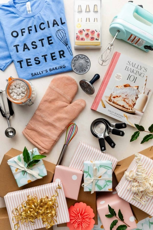 baking items including a shirt, Sally's Baking 101 cookbook, measuring cups, whisks, and an oven mitt with wrapped presents at the bottom.